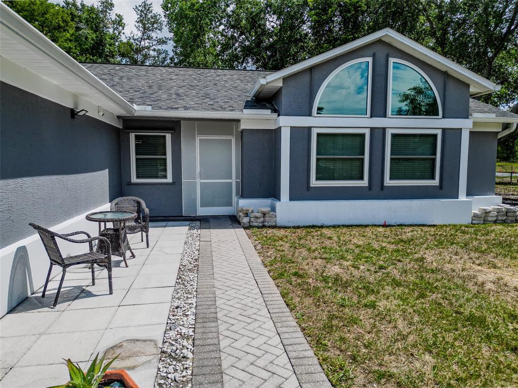 A gray house exterior features a paved patio, a brick walkway, and arched windows — 12090 VENICE DRIVE, SPRING HILL, FL