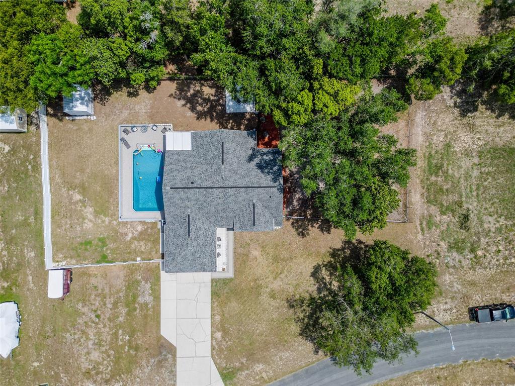 An aerial view shows a house with a swimming pool, driveway, and surrounding trees — 12090 VENICE DRIVE, SPRING HILL, FL