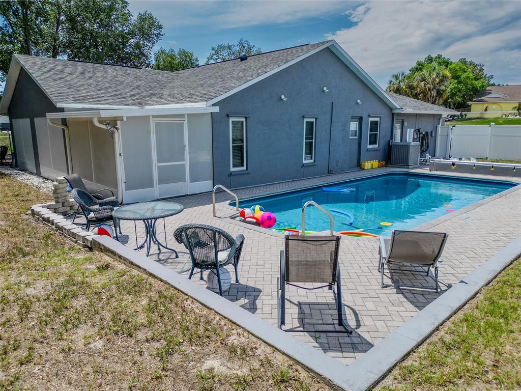 A gray house with a screened-in patio and a paved pool deck in the backyard — 12090 VENICE DRIVE, SPRING HILL, FL