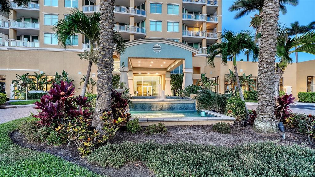 A multi-story building exterior features a covered entrance with a fountain and palm trees — 140 RIVIERA DUNES WAY UNIT 1204, PALMETTO, FL