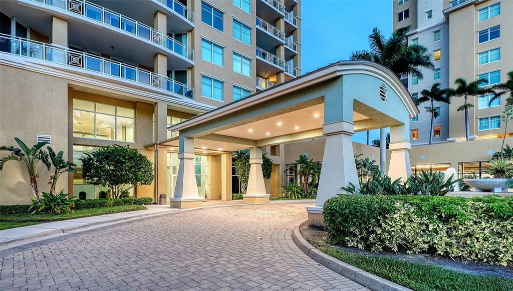 A paved driveway leads to the covered entrance of a multi-story residential building — 140 RIVIERA DUNES WAY UNIT 1204, PALMETTO, FL