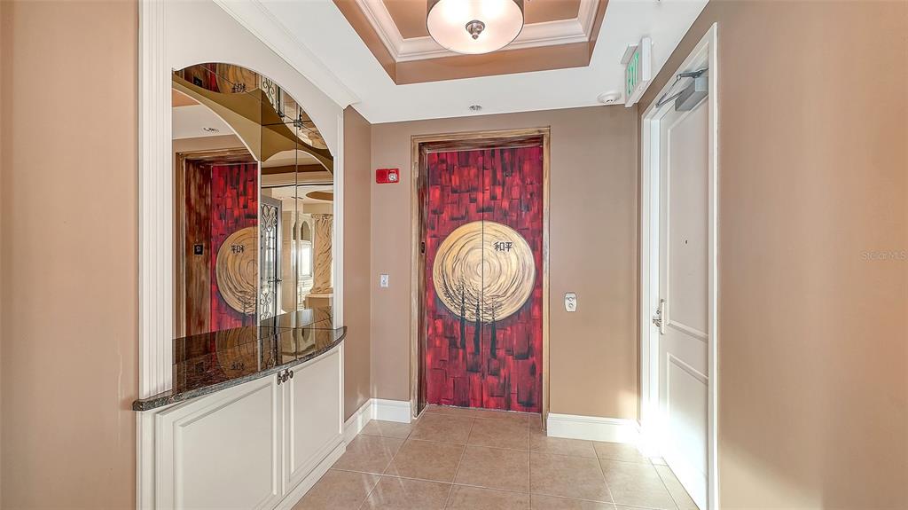 A hallway features a mirrored console, a red elevator door with artwork, and tile flooring — 140 RIVIERA DUNES WAY UNIT 1204, PALMETTO, FL