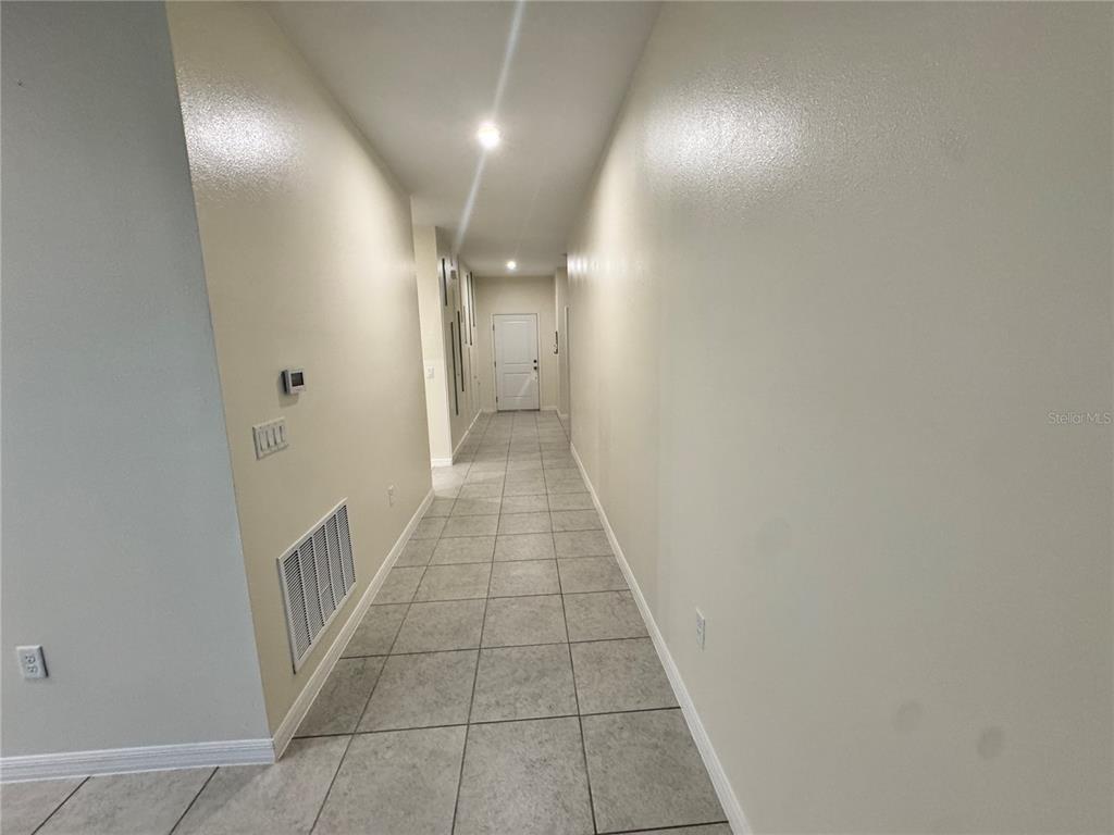 A long hallway with light-colored walls and gray tiled flooring leads to a white door — 34100 CHIPPING SPARROW DRIVE, LEESBURG, FL