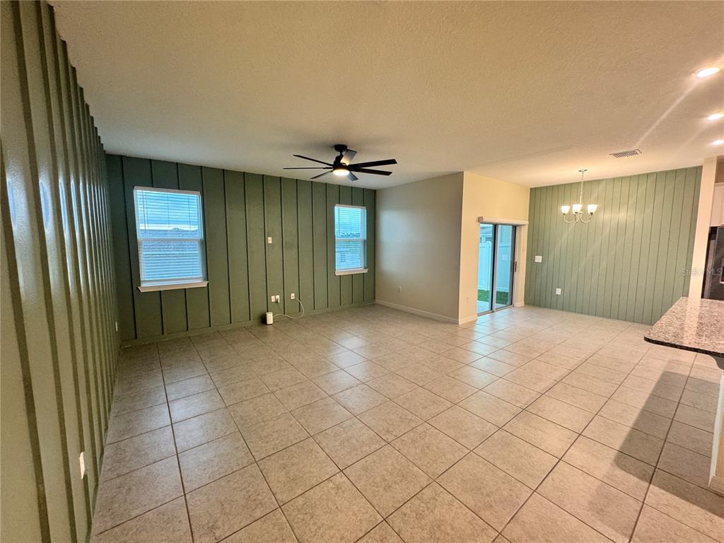 An open-concept living and dining area features sage green vertical paneling and light tile flooring — 34100 CHIPPING SPARROW DRIVE, LEESBURG, FL