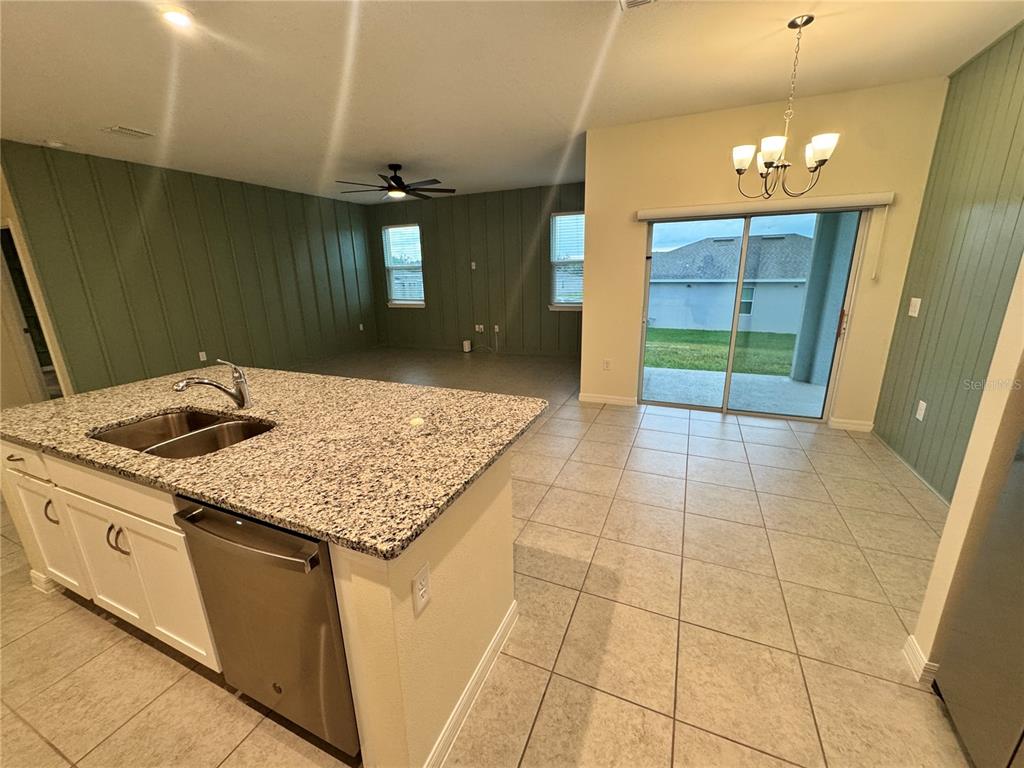 A kitchen island with granite countertops overlooks a tiled dining area and living room — 34100 CHIPPING SPARROW DRIVE, LEESBURG, FL