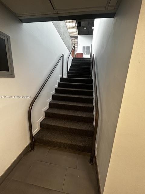 A straight staircase with dark carpeted steps and metal handrails leads to an upper level — 900 W 49th St Suite B001, Hialeah FL 33012, HIALEAH, FL