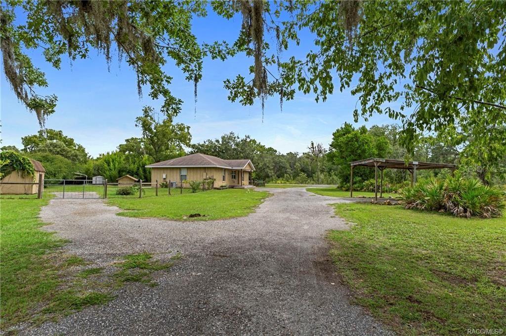A tan house with a gravel driveway, a carport, and a fenced yard with trees — 6185 W OST WEST STREET, HOMOSASSA, FL
