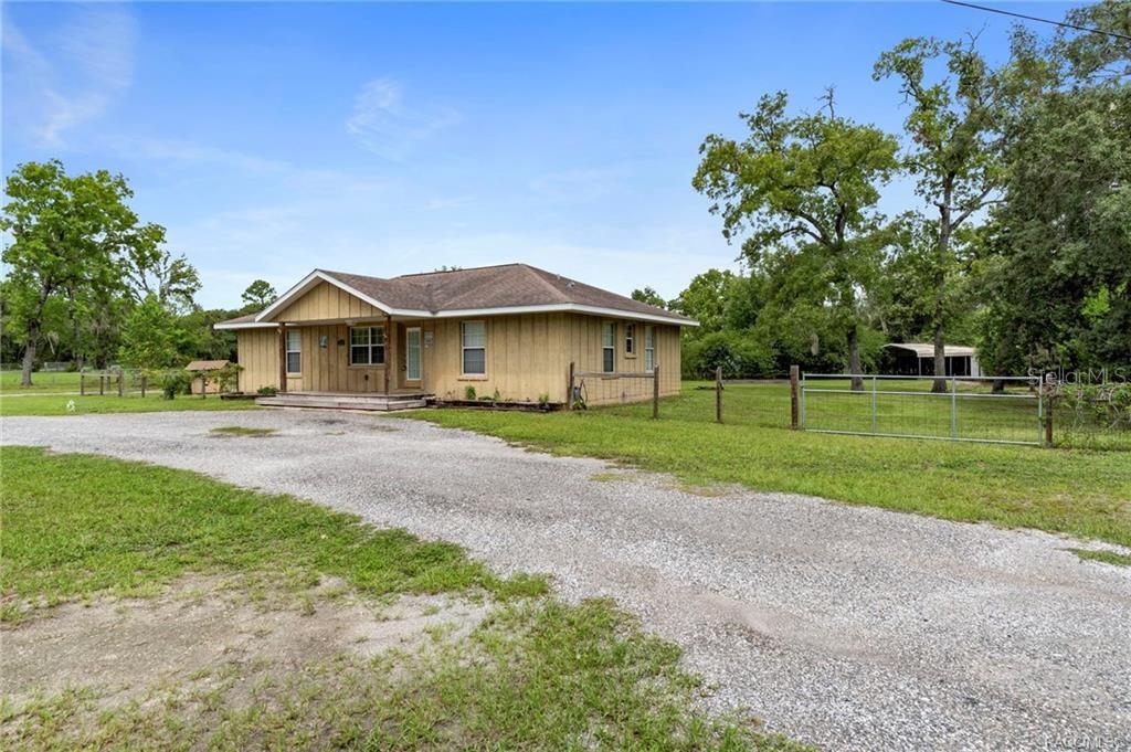 A single-story house with tan vertical siding and a gravel driveway sits on a grassy lot — 6185 W OST WEST STREET, HOMOSASSA, FL