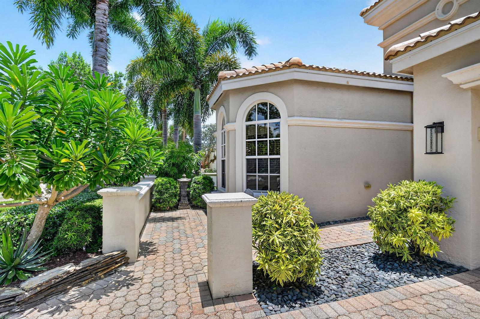 A paved walkway leads past a stucco wall and a window toward a house exterior — 9774 Via Elegante, Wellington FL 33411, WELLINGTON, FL