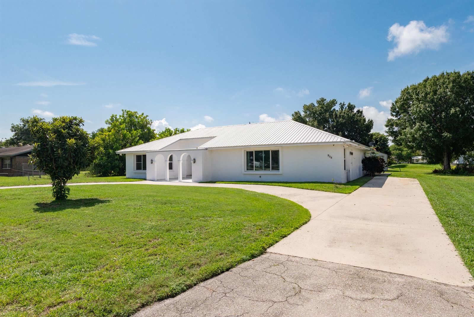 A white single-story house with a metal roof and a concrete driveway sits on grass — 312 De Soto Avenue, Clewiston FL 33440, CLEWISTON, FL