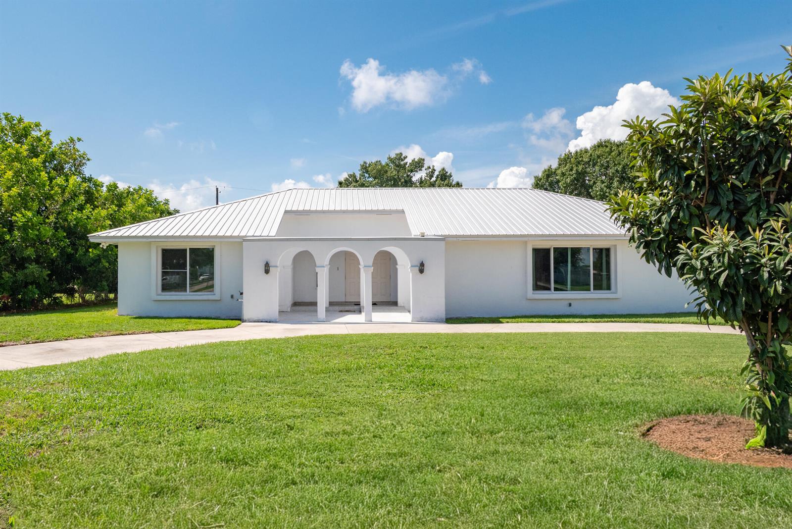 A white single-story house with a metal roof and a three-arched front entryway — 312 De Soto Avenue, Clewiston FL 33440, CLEWISTON, FL