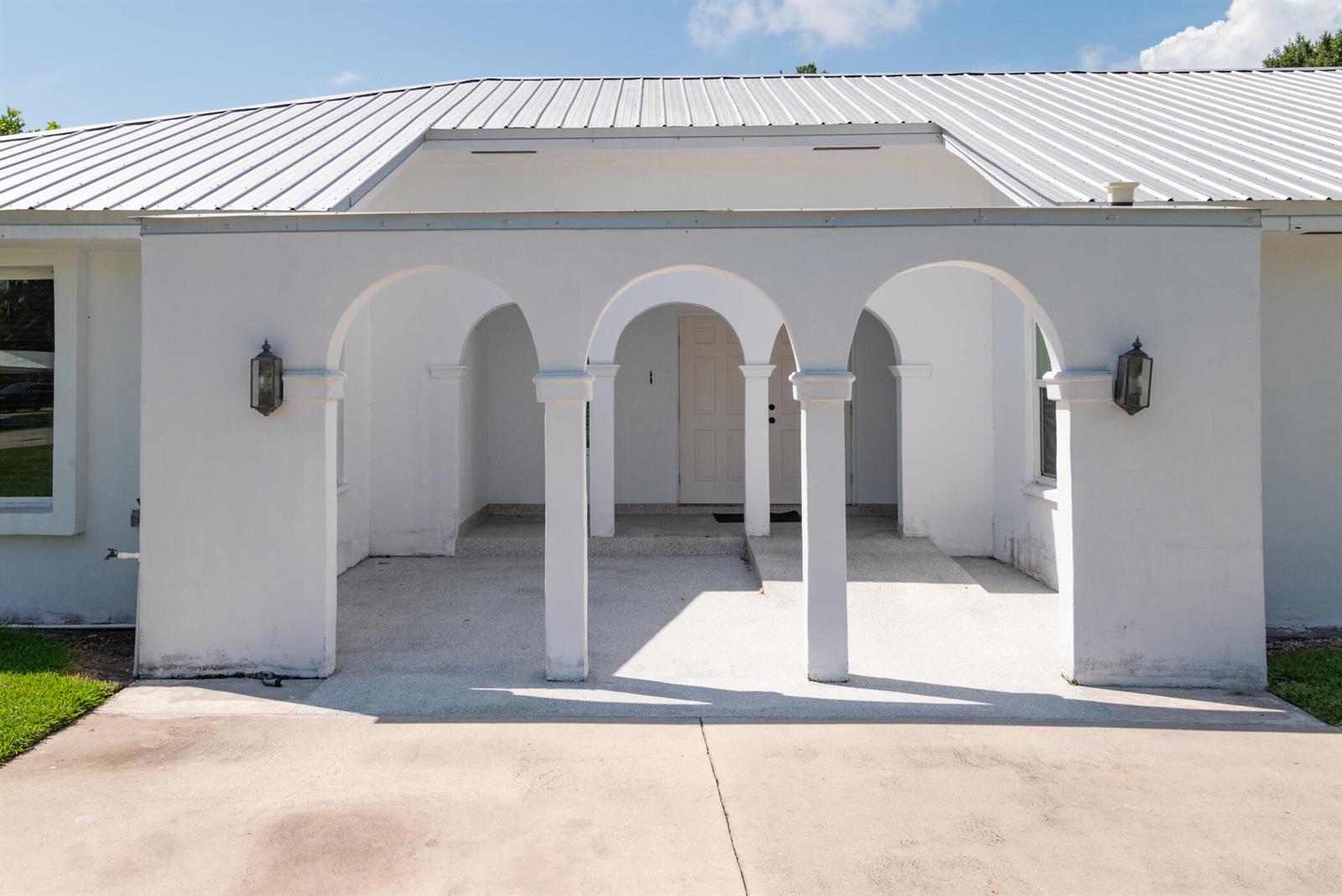 A white house exterior features a covered porch with three arched openings and metal roofing — 312 De Soto Avenue, Clewiston FL 33440, CLEWISTON, FL
