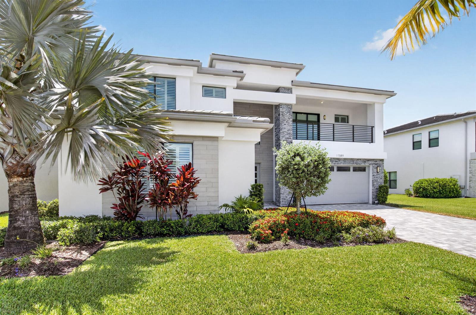A modern two-story house features a white facade, stone accents, a balcony, and landscaped yard — 17089 Rainbow Falls Trail, Boca Raton FL 33496, BOCA RATON, FL