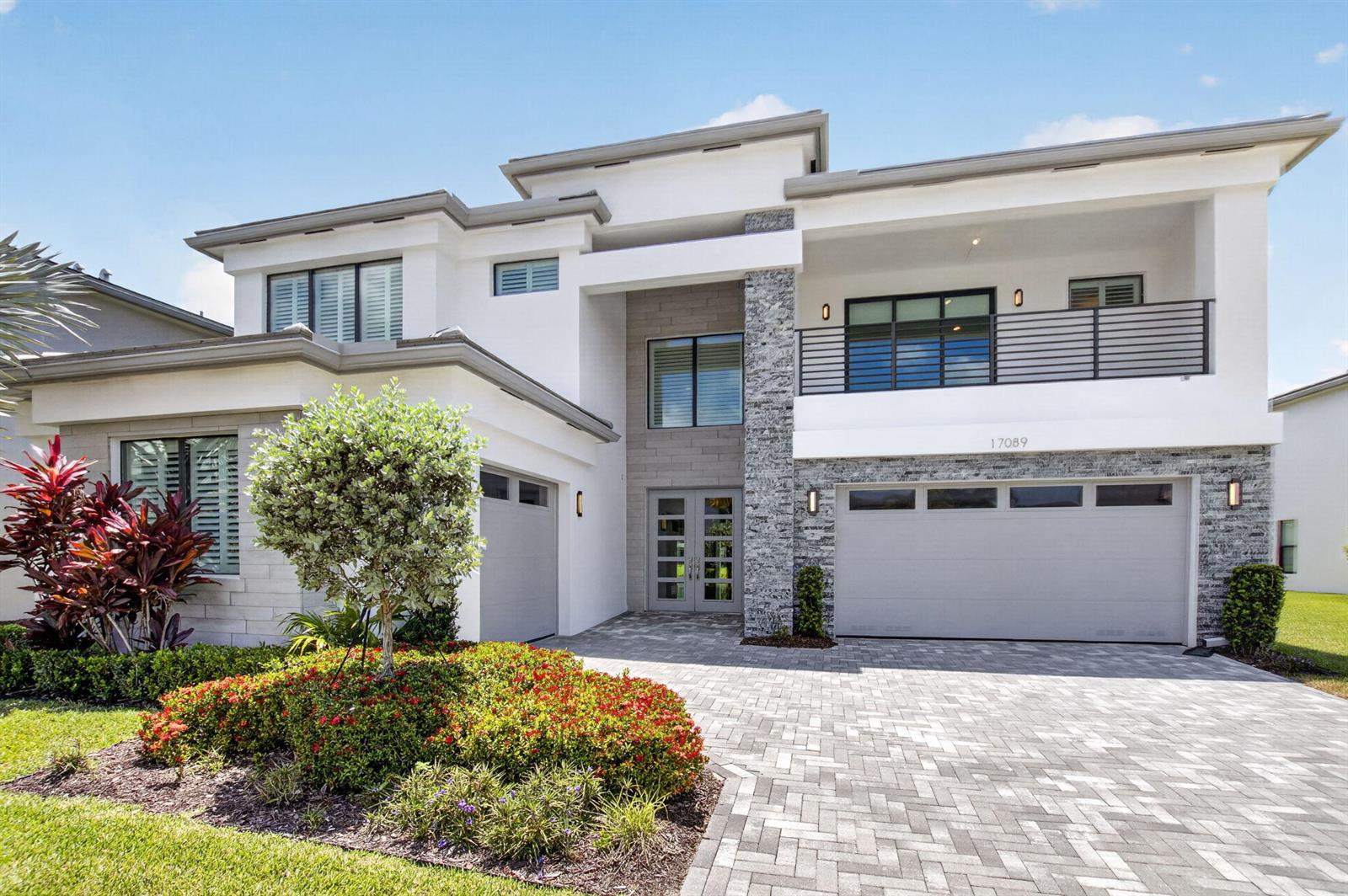 A modern two-story house features a stone facade, a balcony, and a paved driveway — 17089 Rainbow Falls Trail, Boca Raton FL 33496, BOCA RATON, FL