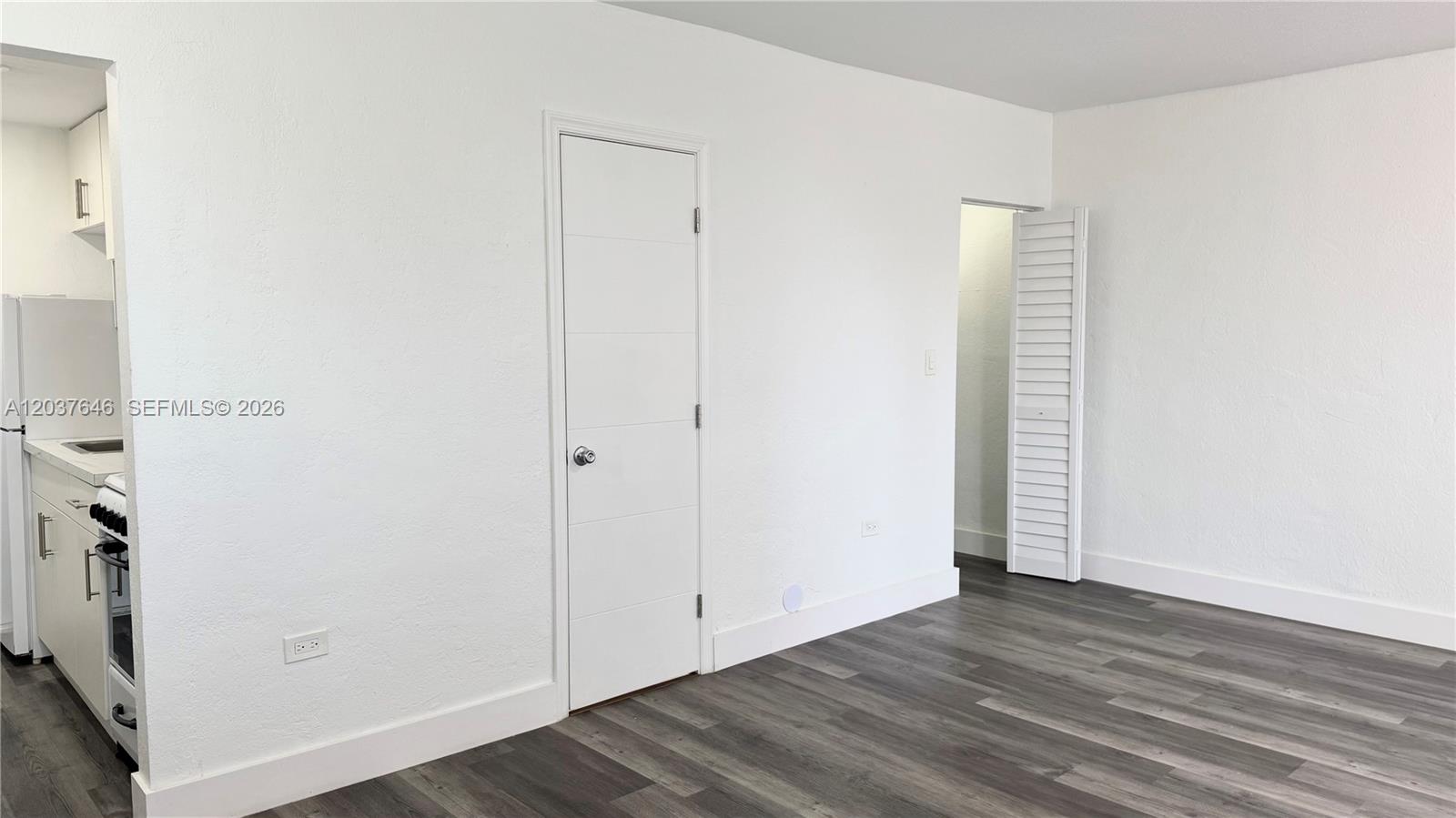 A room with white walls, gray wood-look flooring, a closed door, and an open closet — 7619 Abbott Ave # 9, Miami Beach FL 33141, MIAMI BEACH, FL