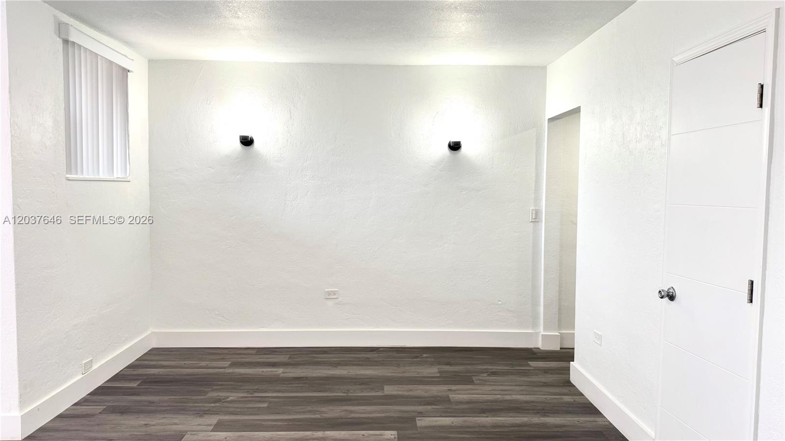 A room with white walls, dark wood-look flooring, two wall sconces, and a white door — 7619 Abbott Ave # 9, Miami Beach FL 33141, MIAMI BEACH, FL