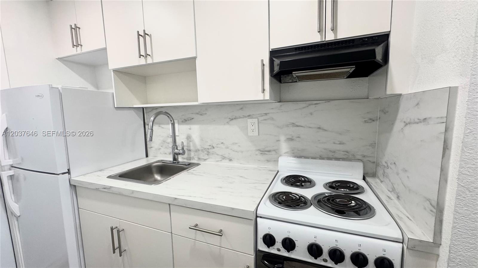 A small kitchen features white cabinets, a marble-patterned backsplash, and a white electric stove — 7619 Abbott Ave # 9, Miami Beach FL 33141, MIAMI BEACH, FL