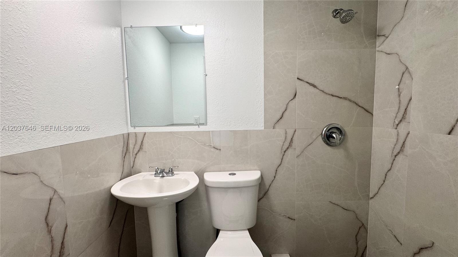 A bathroom features a pedestal sink, a toilet, and a shower with marble-patterned tile walls — 7619 Abbott Ave # 9, Miami Beach FL 33141, MIAMI BEACH, FL