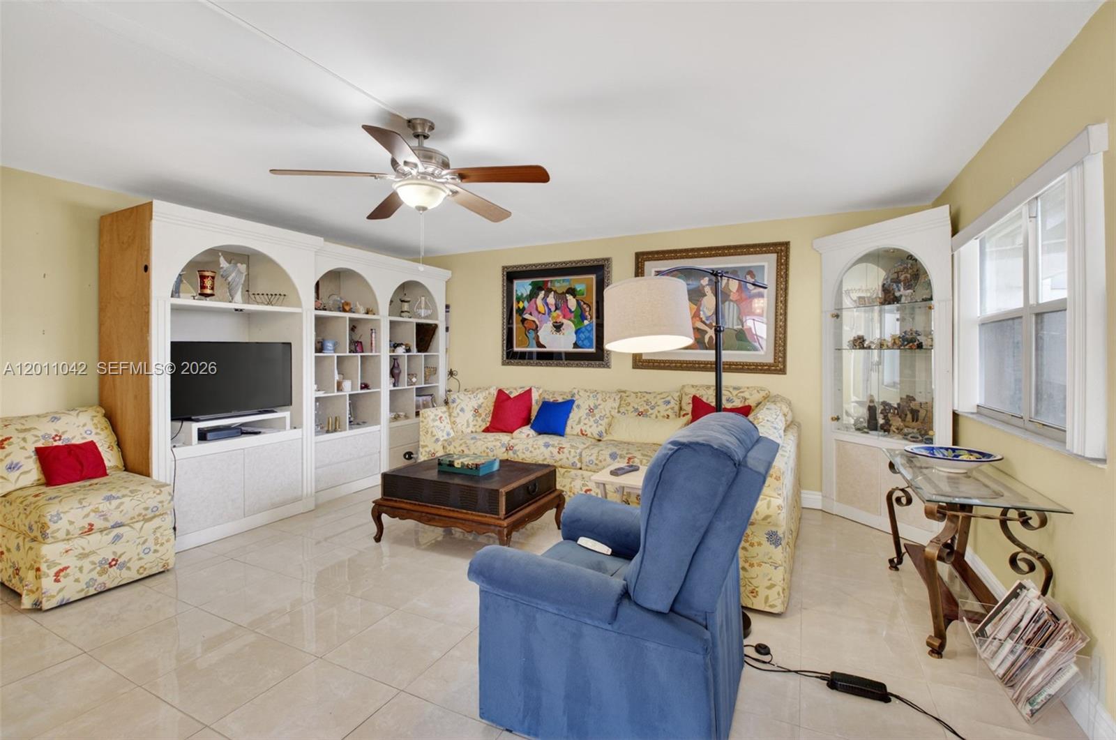 A living room features a floral sofa, a blue recliner, built-in shelving, and tile flooring — 537 Brittany L # 537, Delray Beach FL 33446, DELRAY BEACH, FL