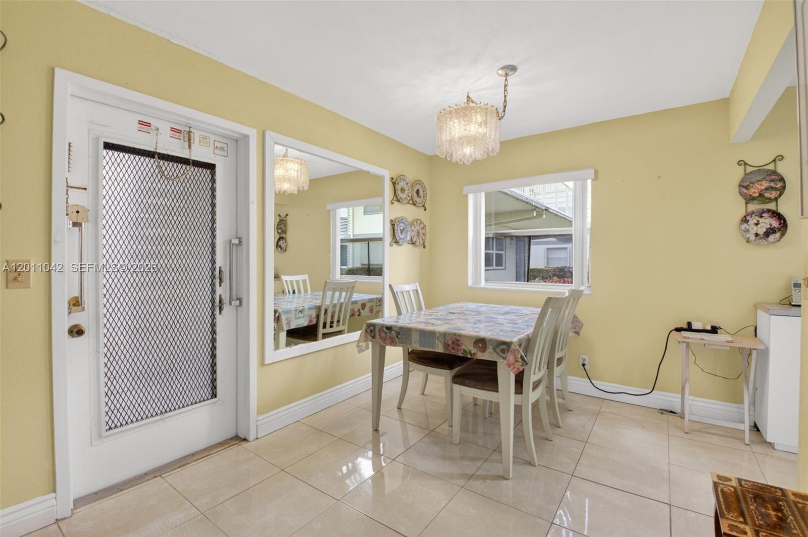 A dining room with yellow walls, tile flooring, a crystal chandelier, and a large mirror — 537 Brittany L # 537, Delray Beach FL 33446, DELRAY BEACH, FL