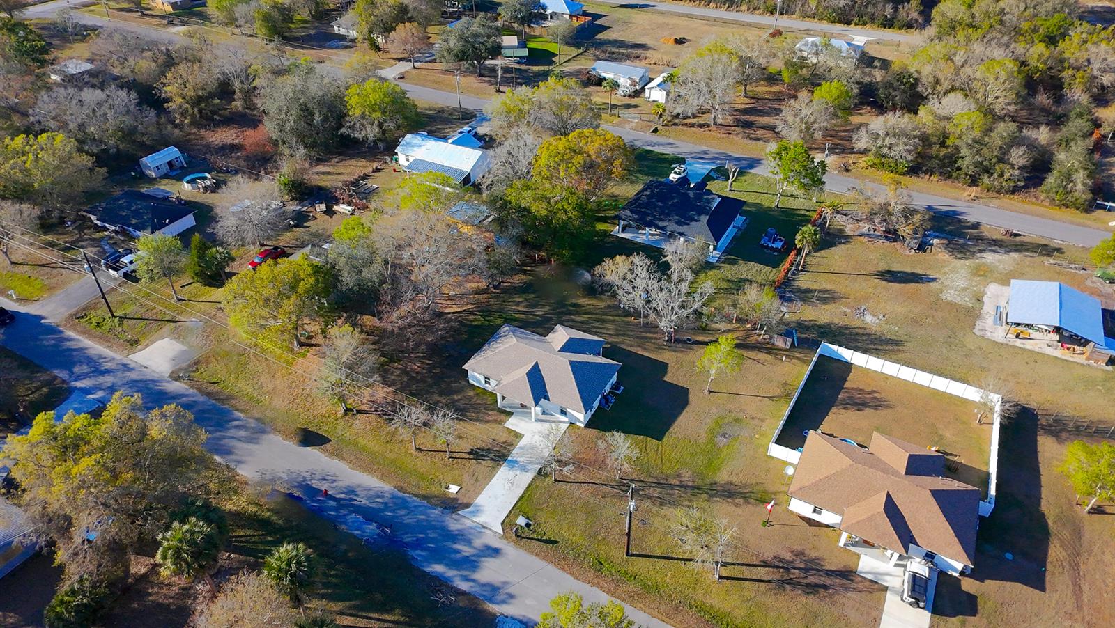 An aerial view shows several houses with driveways, trees, and fenced yards in a rural area — 7757 NW 82nd Court, Okeechobee FL 34972, OKEECHOBEE, FL