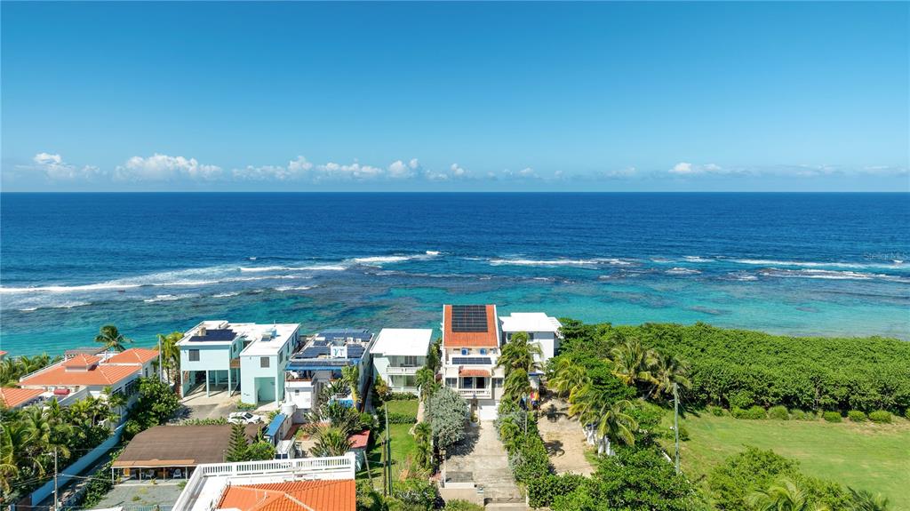 An aerial view shows several coastal houses with solar panels situated along a turquoise ocean — Carr. 466 K5 H3, ISABELA, PR