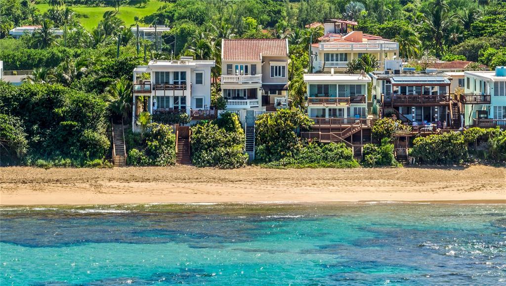 A row of multi-story houses sits on a grassy hill overlooking a sandy beach — Carr. 466 K5 H3, ISABELA, PR
