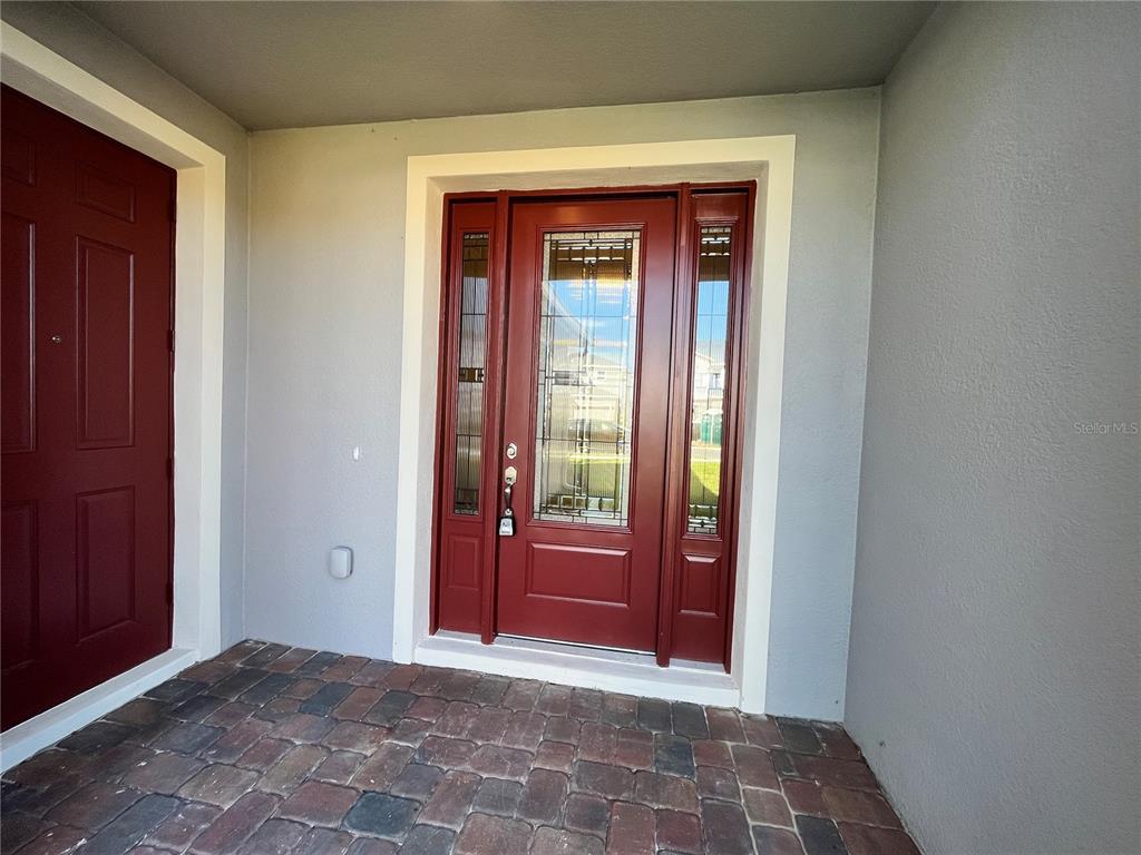 A red front door with glass panels and sidelights sits on a brick porch — 7757 MARSALA STREET, CLERMONT, FL