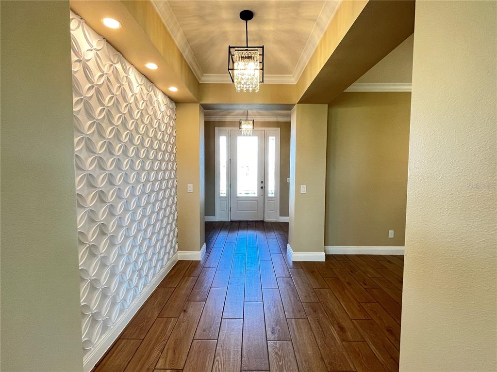 An entryway features a textured accent wall, wood-look tile flooring, and two hanging light fixtures — 7757 MARSALA STREET, CLERMONT, FL