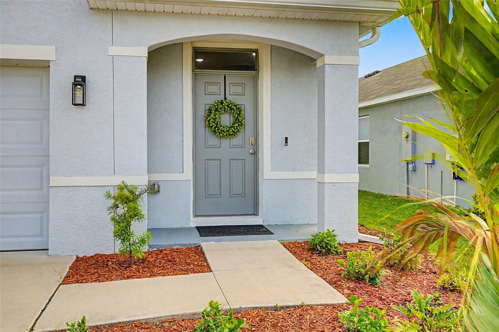 The exterior of a house features a gray front door with a wreath and a walkway — 35686 SUNFLOWER HILL DRIVE, ZEPHYRHILLS, FL