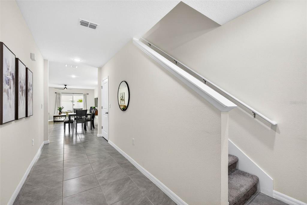 A hallway with tile flooring leads to a dining area past a carpeted staircase — 35686 SUNFLOWER HILL DRIVE, ZEPHYRHILLS, FL