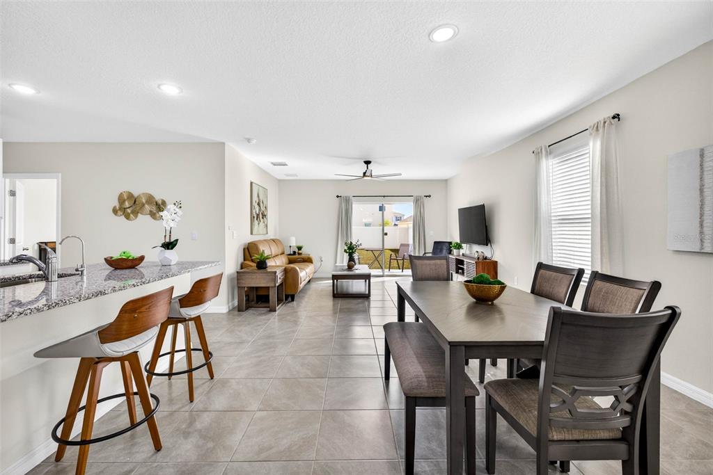An open-concept living and dining area features tile flooring, a kitchen island, and sliding doors — 35686 SUNFLOWER HILL DRIVE, ZEPHYRHILLS, FL