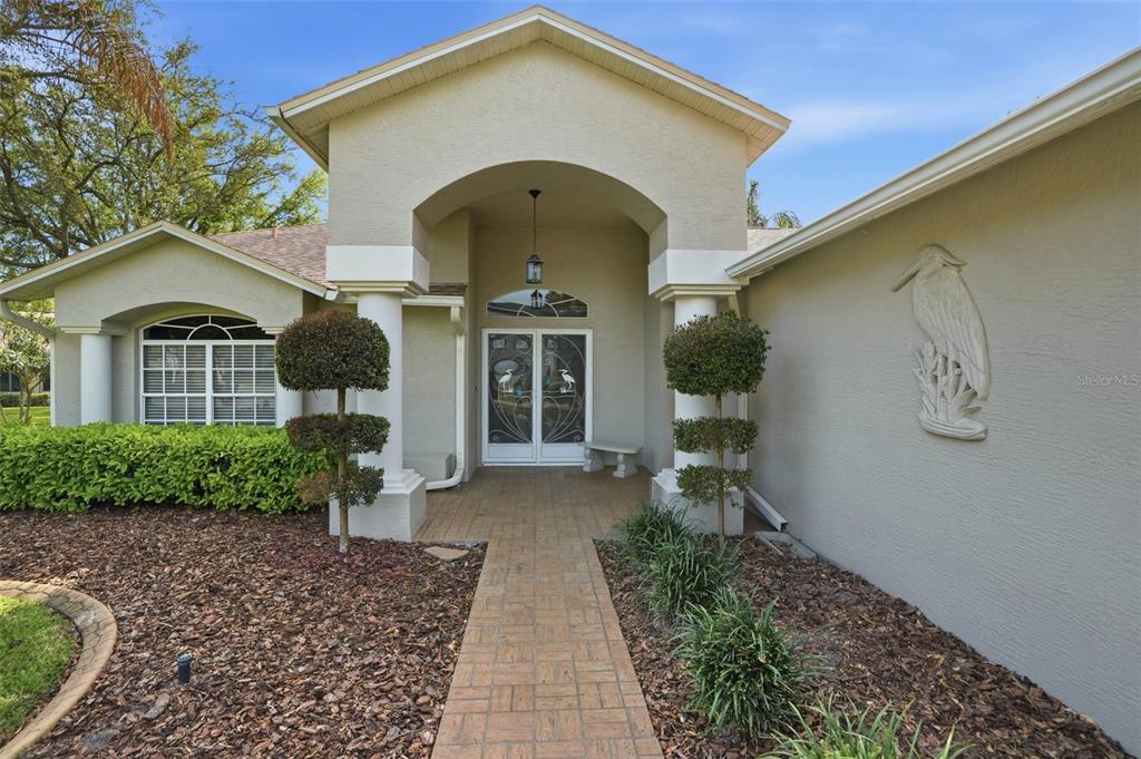 The exterior of a house features a covered entryway with columns and a paved walkway — 18427 WATER LILY LANE, HUDSON, FL