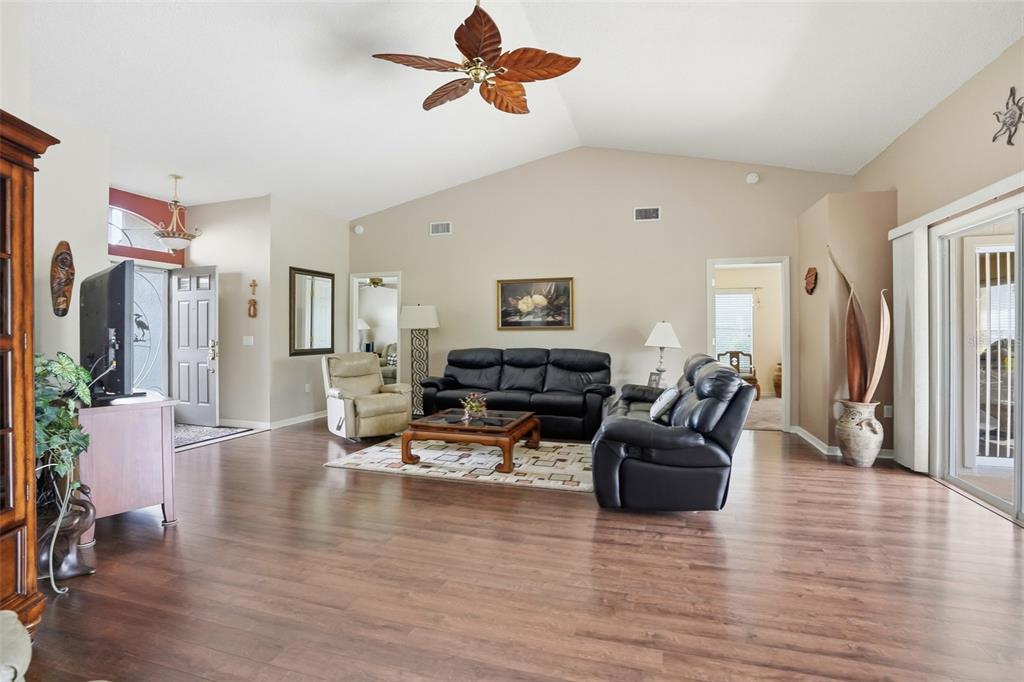 A living room with wood-look flooring, a vaulted ceiling, and black leather furniture — 18427 WATER LILY LANE, HUDSON, FL