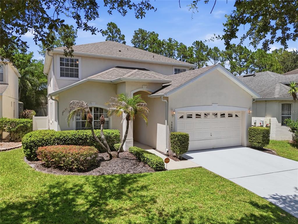 A two-story suburban house with a beige stucco exterior, a two-car garage, and landscaping — 5007 BELLTHORN DRIVE, ORLANDO, FL