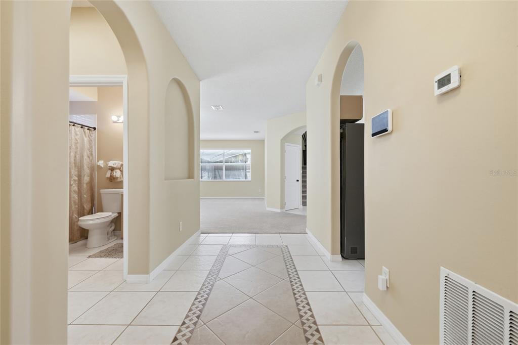 A tiled hallway leads to a carpeted living area with arched doorways and neutral walls — 5007 BELLTHORN DRIVE, ORLANDO, FL