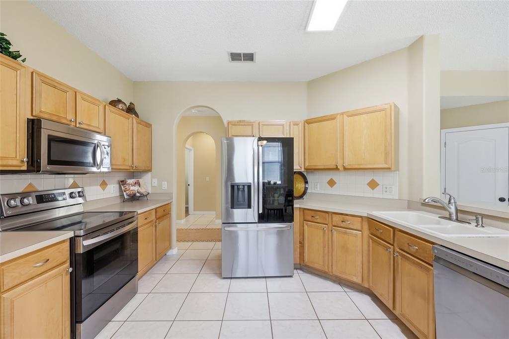 A kitchen features light wood cabinets, stainless steel appliances, white tile floors, and beige walls — 5007 BELLTHORN DRIVE, ORLANDO, FL