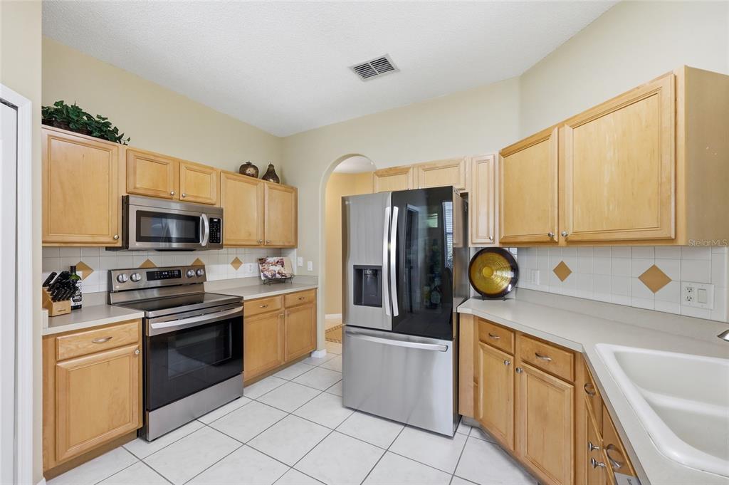 A kitchen with light wood cabinets, stainless steel appliances, white tile backsplash, and tile flooring — 5007 BELLTHORN DRIVE, ORLANDO, FL