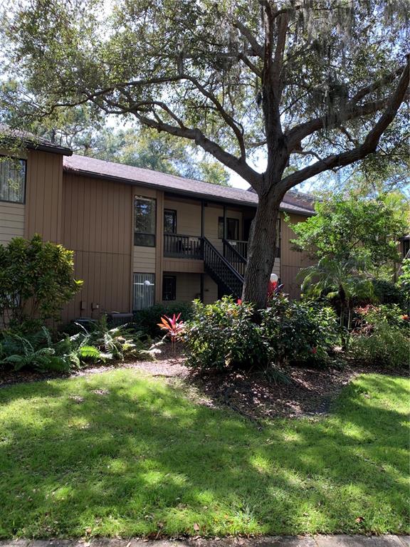 A two-story apartment building with brown siding and a wooden staircase stands behind a tree — 1717 PELICAN COVE ROAD UNIT 333, SARASOTA, FL