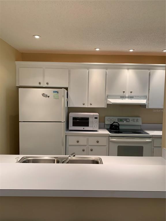 A kitchen features white cabinetry, white appliances, and a double-basin sink with a breakfast bar — 1717 PELICAN COVE ROAD UNIT 333, SARASOTA, FL