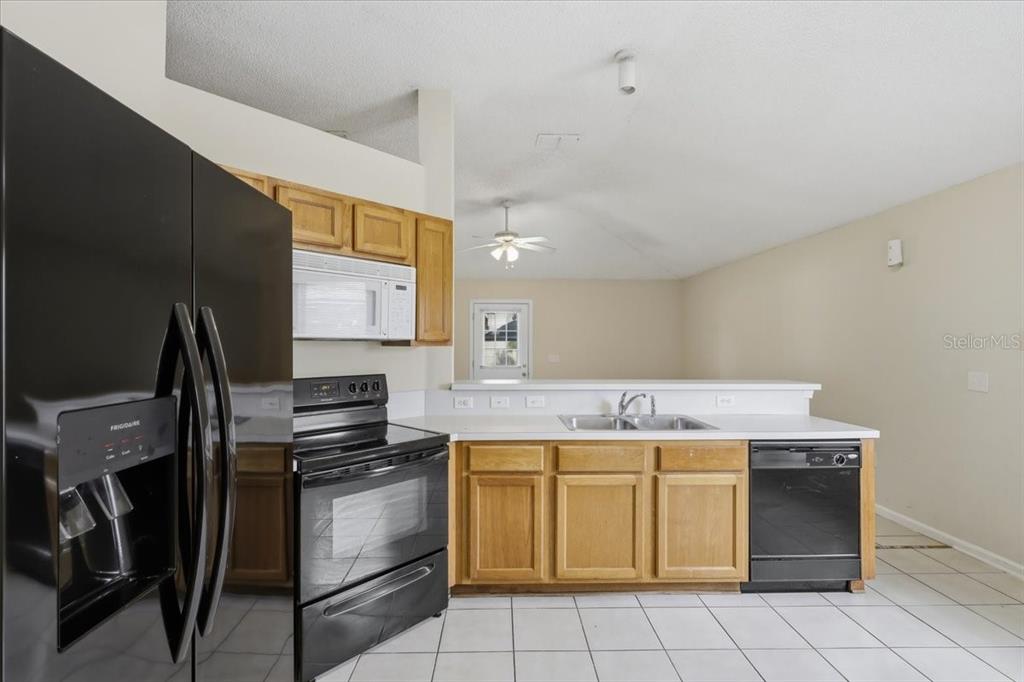 A kitchen with oak cabinets, black appliances, white countertops, and white tile flooring — 3 LOUVET LANE, PALM COAST, FL