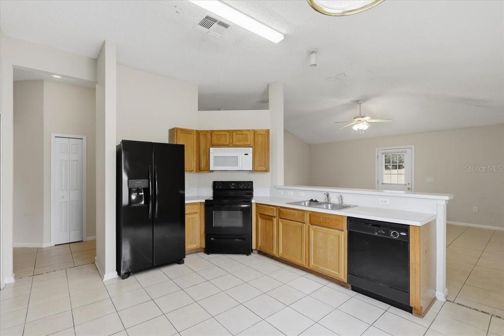 A kitchen features light wood cabinets, black appliances, and white tile flooring — 3 LOUVET LANE, PALM COAST, FL