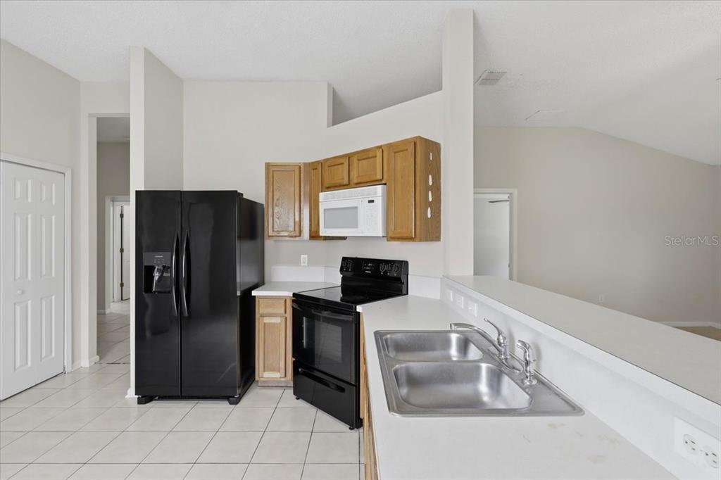 A kitchen features light-colored tile floors, wooden cabinets, black appliances, and a stainless steel sink — 3 LOUVET LANE, PALM COAST, FL