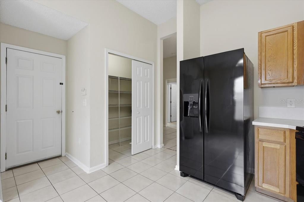 A kitchen features a black refrigerator, light tile flooring, a pantry, and wood cabinetry — 3 LOUVET LANE, PALM COAST, FL