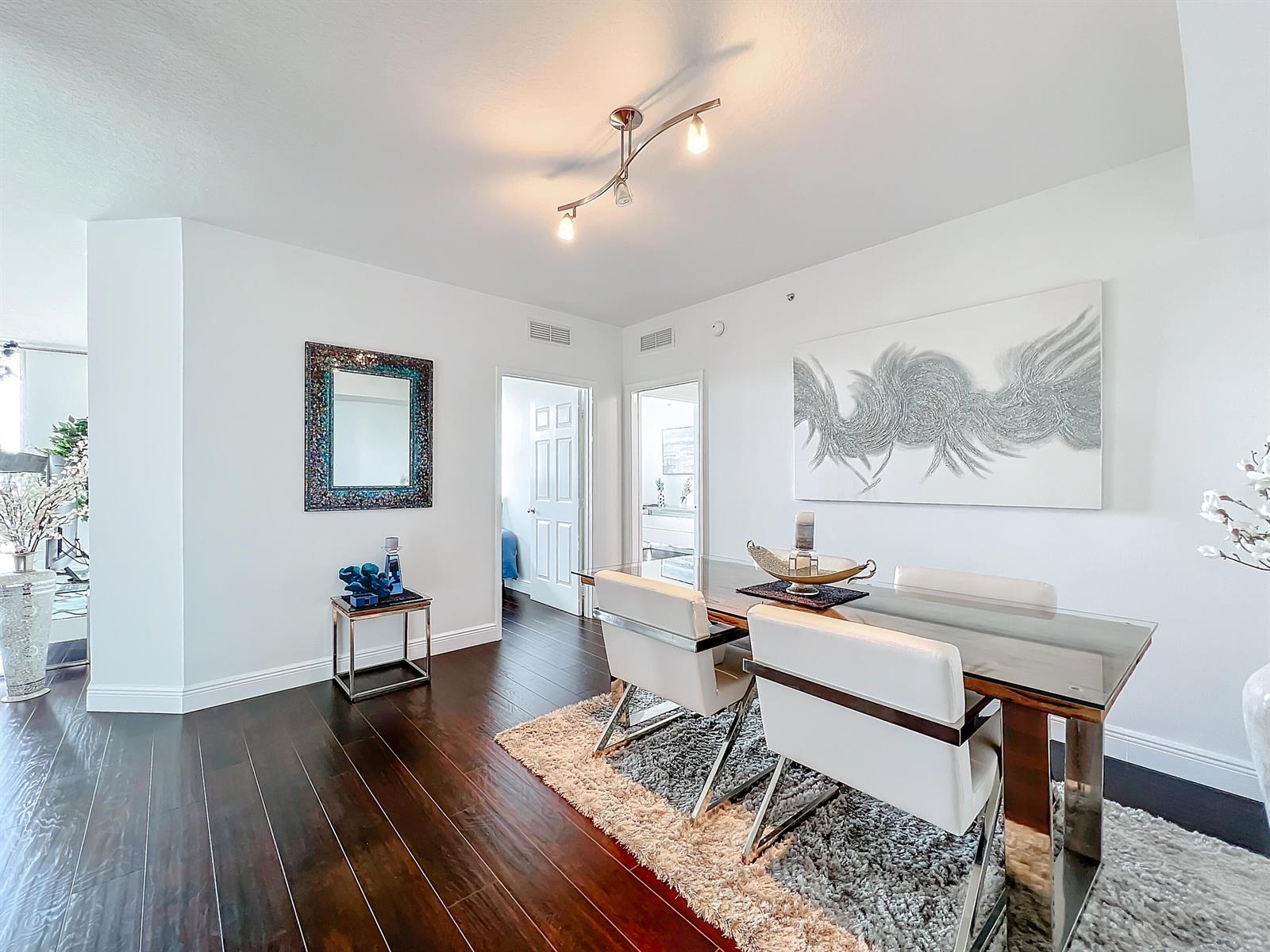 A dining room features a glass table, white chairs, dark wood floors, and wall art — 700 E Boynton Beach Boulevard # 1408, Boynton Beach FL 33435, BOYNTON BEACH, FL