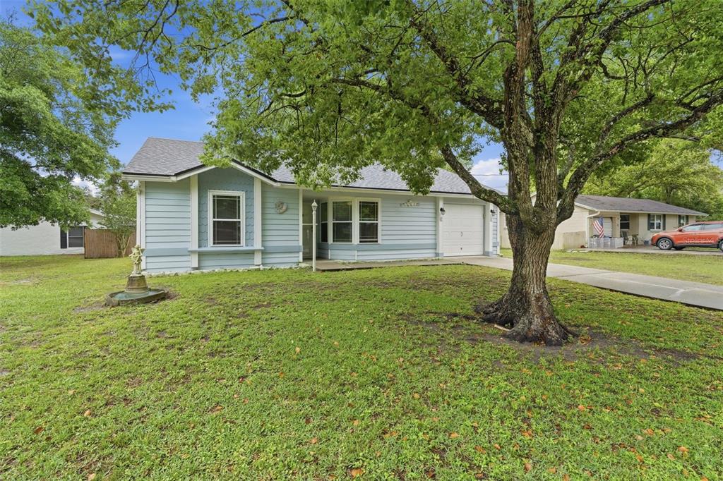 A light blue single-story house with a front lawn, large tree, and attached garage — 61 FLORIDANA ROAD, DEBARY, FL