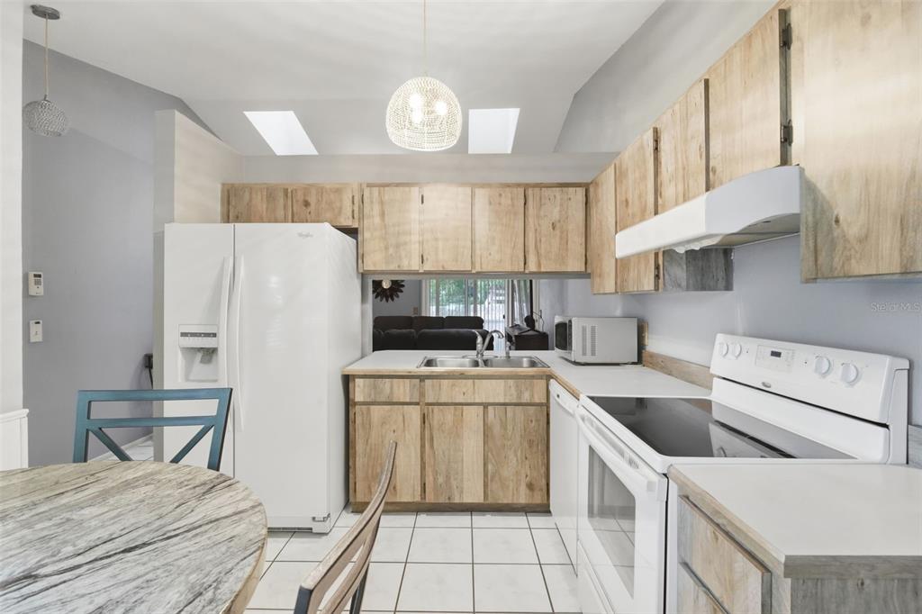 A kitchen features light wood cabinets, white appliances, tile flooring, and a pass-through window — 61 FLORIDANA ROAD, DEBARY, FL