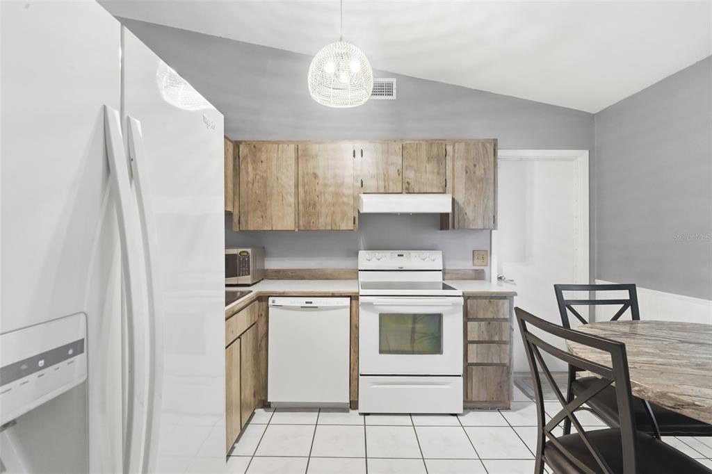 A kitchen features wood-toned cabinets, white appliances, a tiled floor, and a dining table — 61 FLORIDANA ROAD, DEBARY, FL