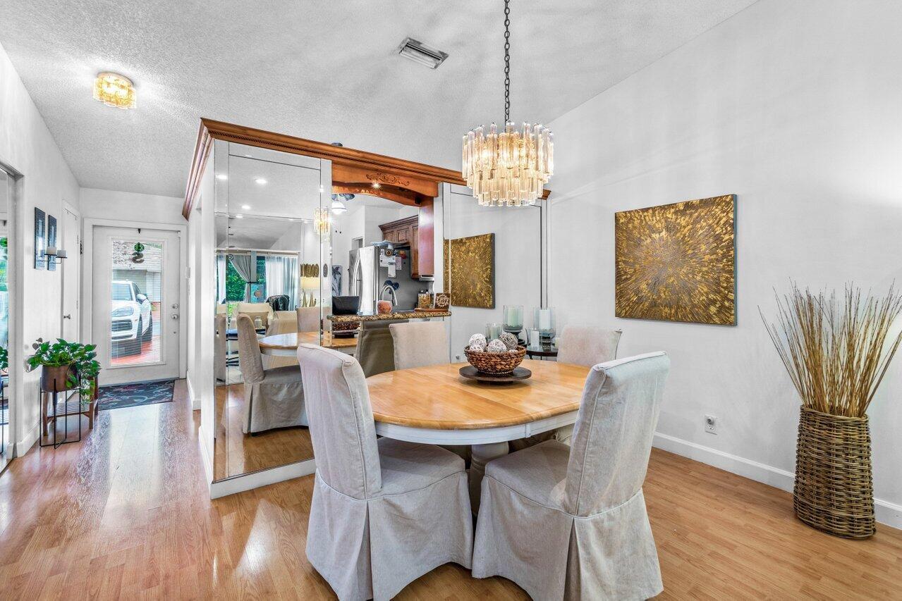A dining room features a wooden table, slipcovered chairs, a crystal chandelier, and mirrored walls — 18855 Candlewick Drive, Boca Raton FL 33496, BOCA RATON, FL