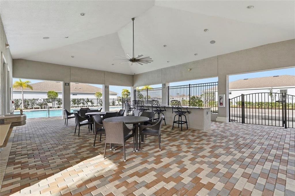 A covered outdoor patio features brick pavers, a bar area, and tables overlooking a pool — 13922 WOODBRIDGE TERRACE, BRADENTON, FL